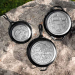 Three cast iron skillets with engraved designs on a stone surface