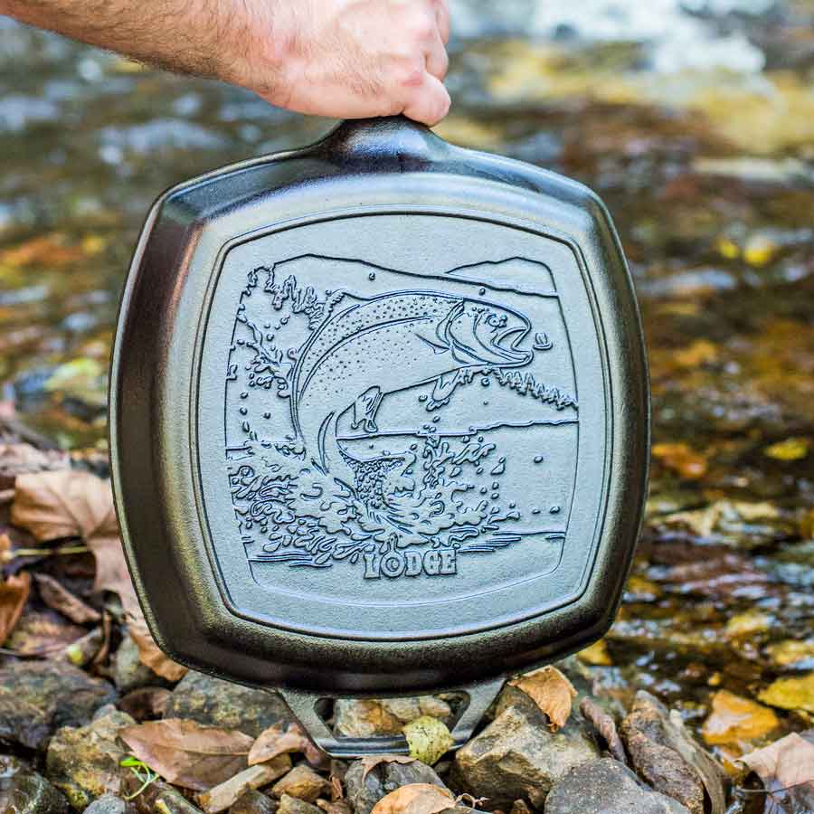 Cast iron skillet with fish design held over a stream.