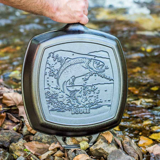 Cast iron skillet with fish design held over a stream.