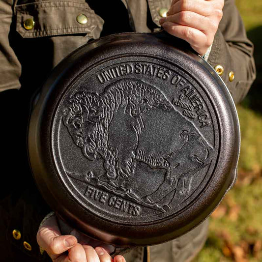 Person holding cast iron skillet display embossed design on the back which features the design from the Buffalo Nickle.