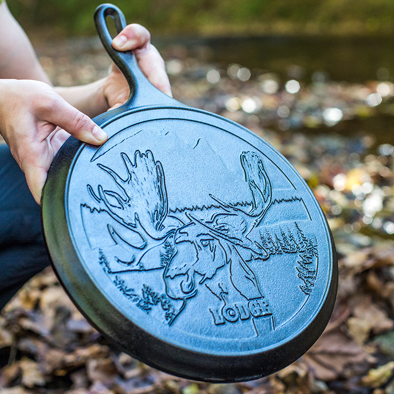 Person holding a cast iron skillet with moose design outdoors.