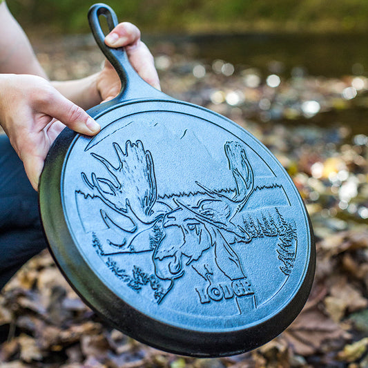 Person holding a cast iron skillet with moose design outdoors.