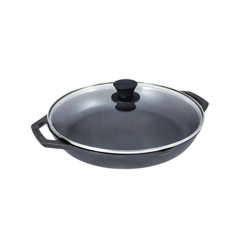 A dual handle cast iron pan with 2 pour spouts topped with a glass lid.