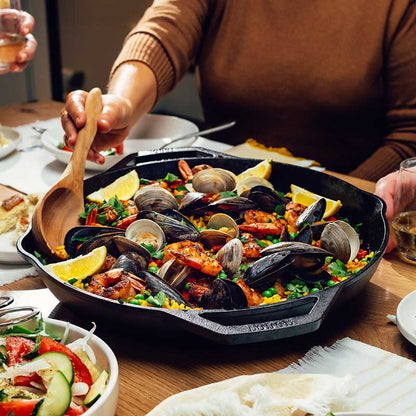 Someone serving seafood paella, freshly prepared and served in pan.