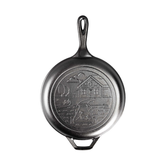 Skillet piece of combo cooker with a long handle, loop handles, and an engraved design of a cabin near a lake with a dog on the dock.