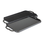 A reversible grill/griddle with one side featuring grooves for grilling and the other side flat, both sides Seasoned with a black seasoning, with lifted handles on the sides.
