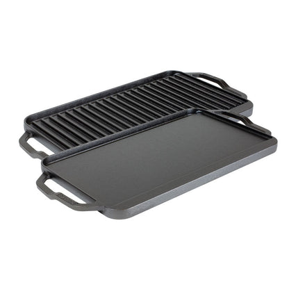 A reversible grill/griddle with one side featuring grooves for grilling and the other side flat, both sides Seasoned with a black seasoning, with lifted handles on the sides.