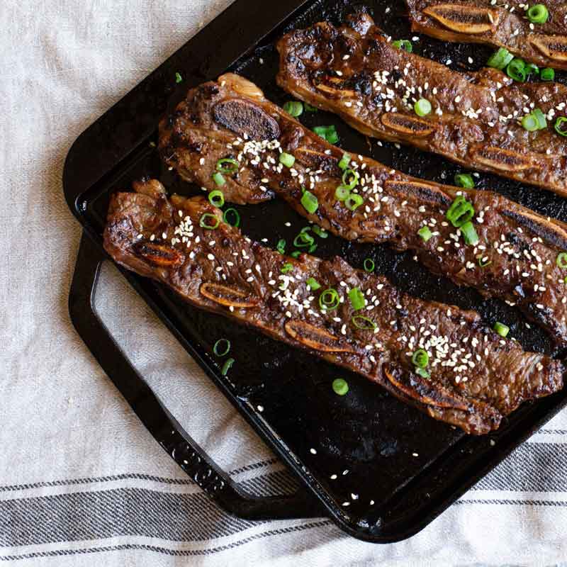 Short ribs seasoned with sesame seeds and green onion prepared on griddle.