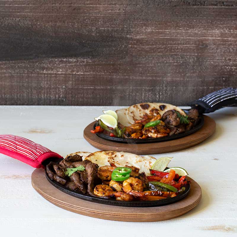 Fajita meal served fresh with griddle set including steak, shrimp, veggies, limes, and tortillas.