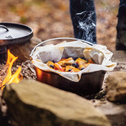 Someone cooking with dutch oven near fire, using liner to protect cookware from food and cleaning.