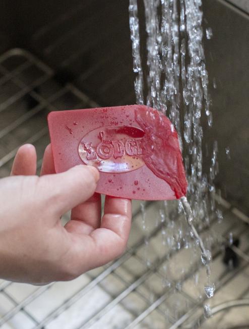 Someone rinsing off the red pan scraper after use on pan.