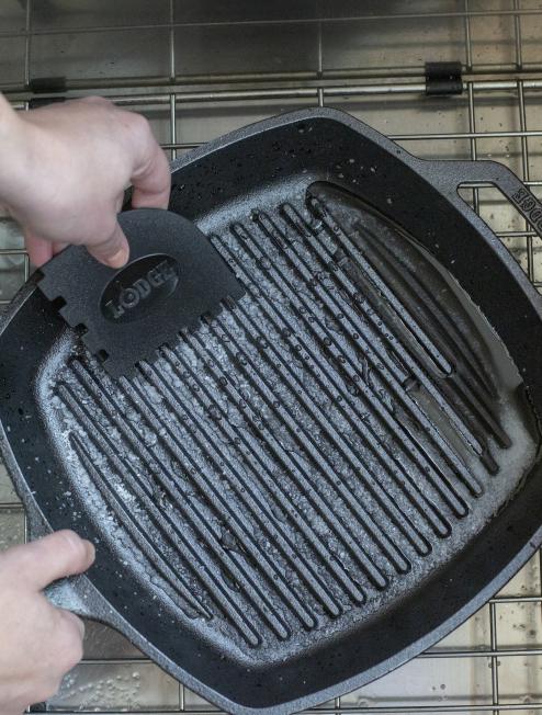 Someone using scrapper to clean grill pan.