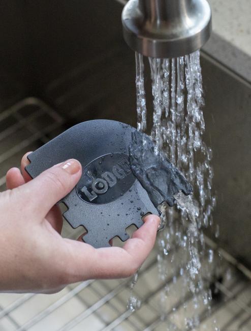 Someone rinsing black scraper under running water.