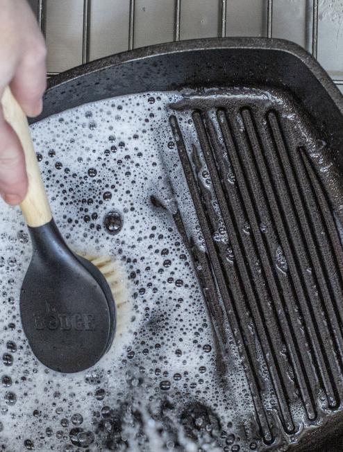 Someone scrubbing their cast iron grill pan with brush and soapy water.