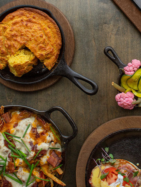 A variety of freshly made dishes served in cast iron on wood underliner.