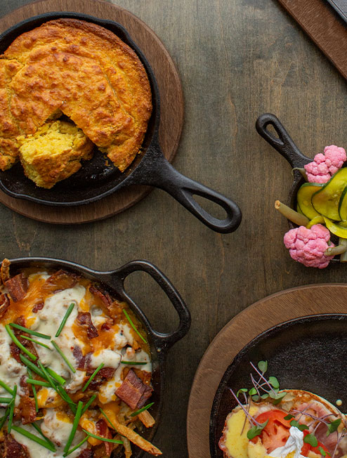 A variety of freshly made dishes served in cast iron on wood underliner.