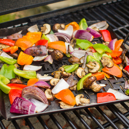 Close-up of veggies roasting in grill basket over charcoal grill.