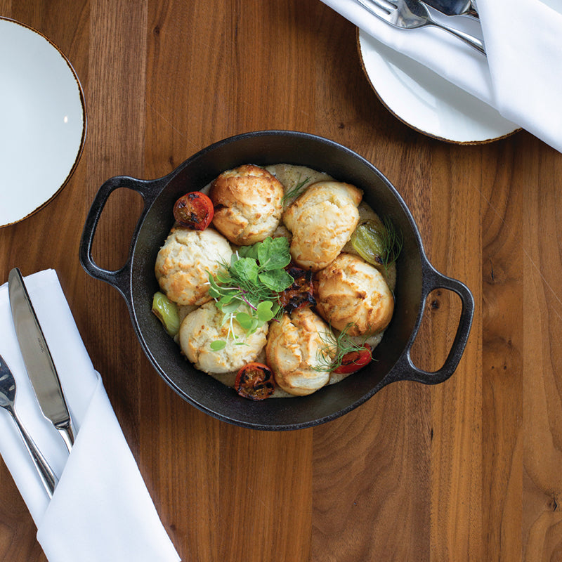 A savory stew topped with dumplings, served at table in pan.