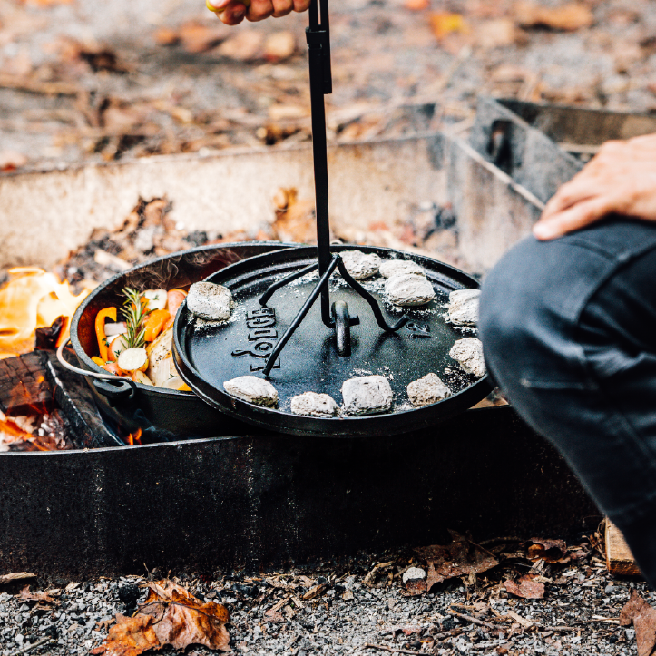 Someone using the Lodge Deluxe Lid Lifter to take off lid on dutch oven.