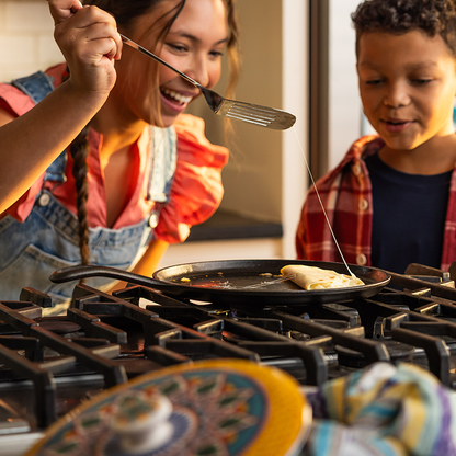 Woman and child cooking a quesadilla together on a stovetop with griddle.