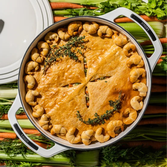 Our croissant-crust chicken pot pie, prepared in dutch oven, on table of celery and carrots.